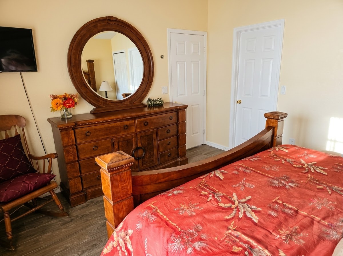 Master bedroom with wooden dresser, round mirror and wall-mounted TV
